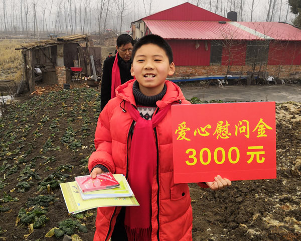 商會慰問團小成員王睿手舉慰問金KT板和自帶的慰問寫字練習本，正懷著贈人玫瑰手留余香的感恩之心，快步走向特困戶家中